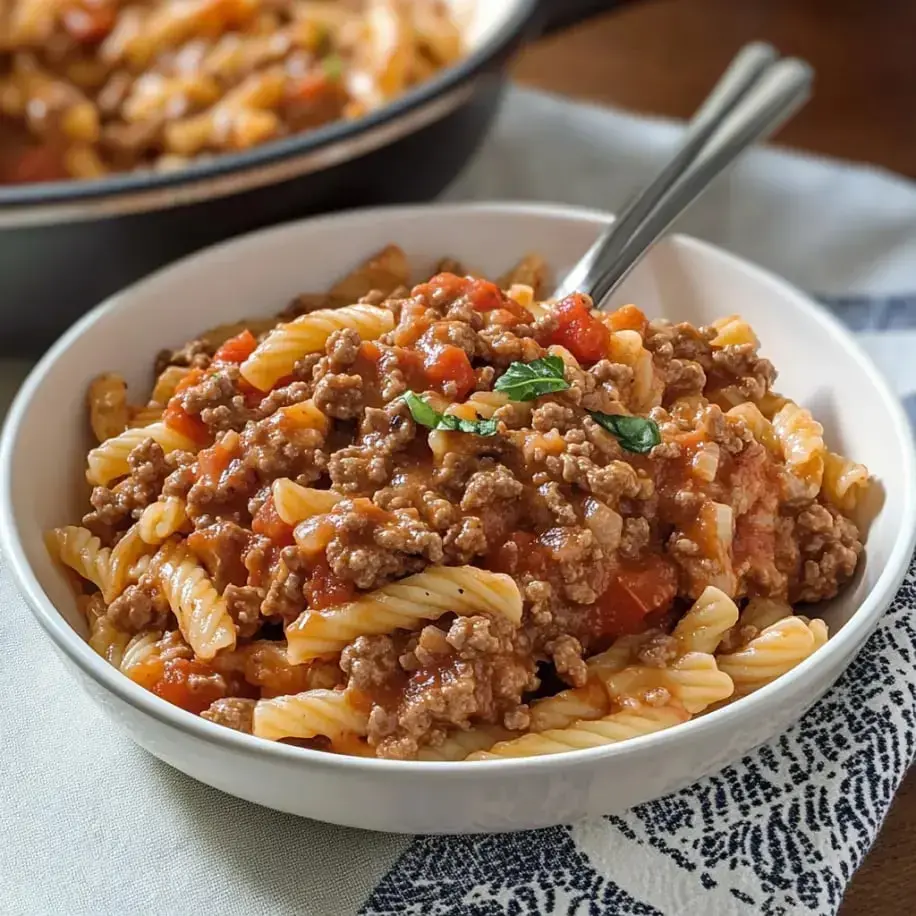 A bowl of pasta with ground beef in a creamy tomato sauce, topped with basil.
