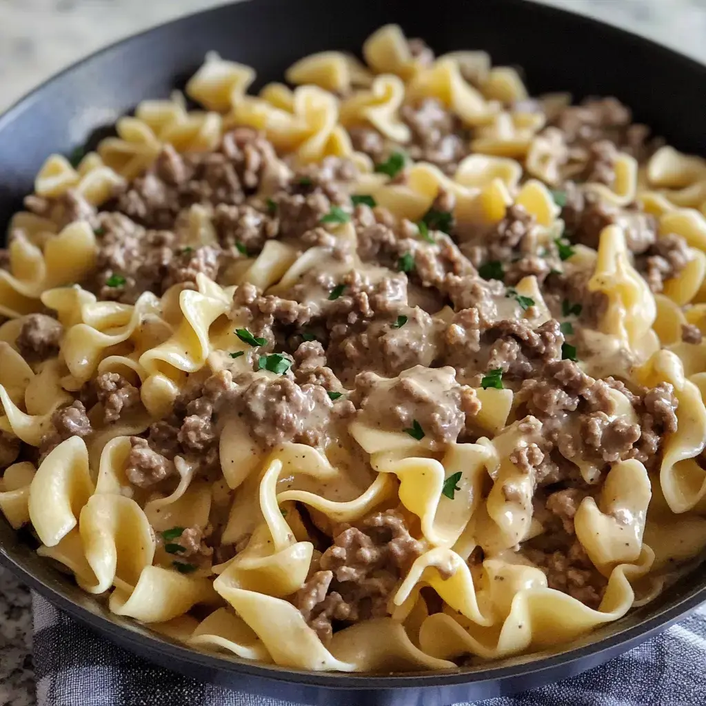 Egg noodles covered in a rich, creamy sauce with ground beef, sprinkled with parsley in a skillet.