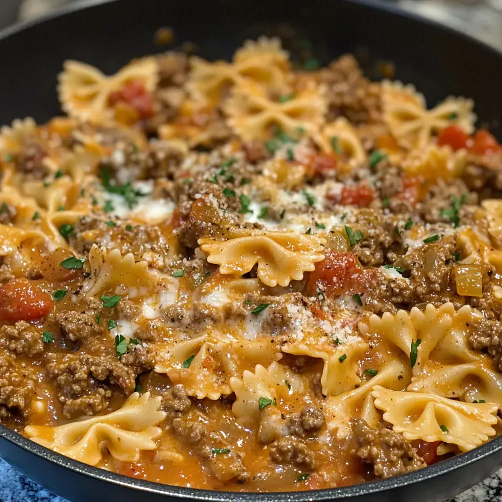 A large pan filled with bowtie pasta combined with ground beef, diced tomatoes, and finished with fresh herbs and melted cheese.