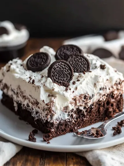 A slice of chocolate cake with white frosting and two chocolate cookies on top.