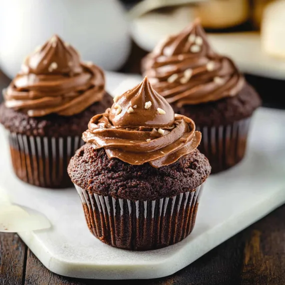 Three cupcakes topped with chocolate frosting and white sprinkles.