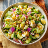 A big bowl packed with cucumbers, red onion, eggs, and colorful peppers.