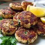 A dish of chicken patties served with lemon wedges.