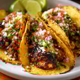 A plate of tacos topped with fresh salsa and lime wedges.