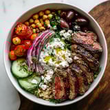 A bowl filled with fresh veggies, tender steak, and creamy toppings.
